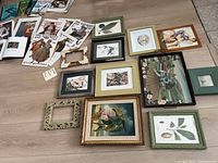 Photo of assortment of framed and unframed art and illustrations on floor including botanical prints, floral paintings, vintage magazine covers, and empty frames.