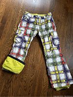 Front view of Burton Dryride pants showing multicolor checkered pattern and yellow snow gaiter on bottom cuff