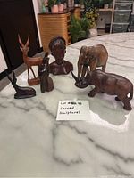 Six carved wooden sculptures placed on a marble surface, showing all pieces including bust and animals.