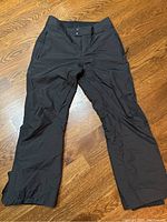 Full front view of black Columbia ski pants on wood floor showing overall condition and style.