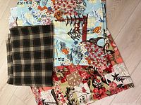 Lot of three fabric pieces: plaid, oriental, and Hawaiian prints neatly folded on wooden floor