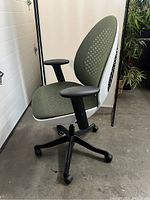 Side view of ergonomic office chair highlighting mesh fabric seat and backrest, white frame, black armrests and base with caster wheels.