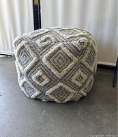 Overall view of square pouf ottoman on floor showing geometric pattern dimensions and texture.
