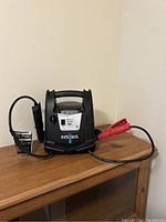 Full view of jump starter on wooden surface showing handle, black and red clamp cables, black casing.