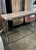 Sideboard showing faux grey wood rectangular top and chrome open metal base with angular curved crossbars