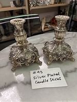 Pair of silver plated candle holders with ornate detailing on a marble surface.