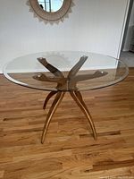 Full view of the round glass top dining table on sculptural wooden legs showing the clear beveled glass top and overall shape.