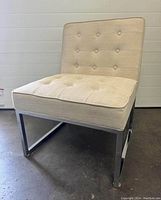 Front view of an ivory fabric occasional chair with button tufted seat and backrest, chrome metal base visible.