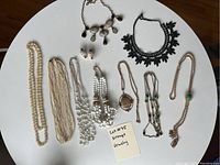 Top down photo of 7 necklaces, bracelet and earrings on white background