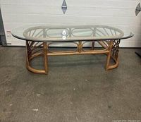 Full view of the oval glass coffee table on a rattan base, showing the entire table structure and glass top.