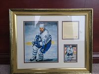 Full view of framed picture showing large painted image of Wendel Clark skating, small photograph below, and a plaque with text to right within a gold frame.