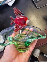 Side view of ashtray held in hand showing green swirls and red fish with fins and detailed eyes