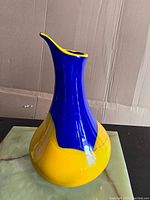 Front angled view showing full vase with bulbous yellow base and tall blue neck with yellow rim edge.