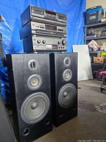 Overall view of the Technics audio components stacked with the two black floor-standing speakers in front showing speaker drivers.