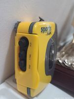 Side view of yellow SPORTS by GPX cassette walkman showing controls for play, fast forward, and stop.