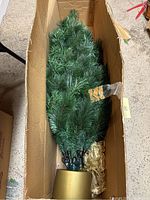 Photo of green artificial Christmas tree folded and packed inside original cardboard box.