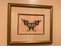 Full view of the framed butterfly embroidery piece with gold frame and beige fabric mat.