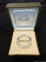 Front view of scarf slide inside Christofle Paris box showing concentric ring design
