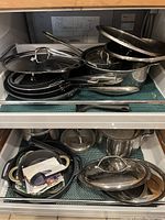 Top drawer view showing mixed stainless pots, nonstick pans, lids and spatula