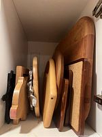 All cutting and serving boards arranged upright in a cabinet showing different shapes and sizes including wood and cork surfaces.