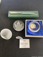 Top view of all items including Kirk Stieff letter opener in box, Baccarat leaf design paperweight, flower etched crystal paperweight, frosted fish paperweight, and Hoya clock paperweight in box with blue satin lining.