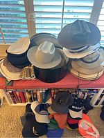 Overview of the collection showing stacked felt hats, flat caps and multiple baseball caps on lower shelf.