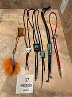 Six items arranged on marble surface: five bolo ties and one hair comb