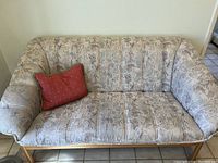 Front view of small love seat sofa with patterned upholstery and red pillow