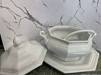 Photo of the white stoneware tureen with lid beside the serving platter and spoon