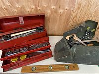 Open red metal toolbox top view showing assorted tools including tape tins and ratchet wrench.