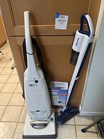 Pair of vacuum cleaners: Miele S184 upright and ReadiVac cordless, with Miele manual visible.