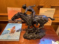 Sculpture with three art books positioned behind on wooden surface