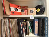 Shelf containing multiple vintage vinyl records including 45s in paper sleeves and LPs arranged side by side
