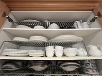 Three shelf cupboard filled with Wedgwood china dishes showing plates, cups, bowls, creamer, and sugar bowl.