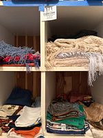 Shelf compartments showing folded scarf stacks: crocheted cream scarves with fringe on top right, assorted knitted and pashmina scarves below