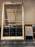 Barn window frame with distressed white paint on one side and metal bars separating glass panes, with washboard beside it on couch
