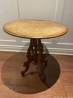 Full view of the antique round pedestal table showing carved wooden legs and sturdy construction