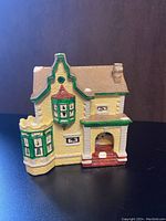 Front and side view of the yellow Christmas village house with green and red accents, showing detailed windows, chimney and porch on a dark background.