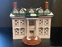 Front view of pink mansion house showing detailed pink walls, white snow accents on roof and porch columns, brick chimneys, and textured windows.