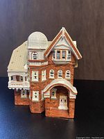 Front angled view of Department 56 Christmas village house showing brick facade, arched entryway, turret, and snow-tipped roof.