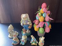 View of all Easter decorations including five small bunny figurines, one larger bunny figurine, a decorative Easter egg topiary, and one Precious Moments figurine