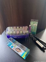 Photo of Conair hot rollers in purple case, assorted rollers in pastel colors, hairpins, plastic hair twists in packaging, and two metal head massagers placed on top