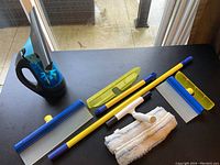 Mgico Polti cordless window cleaner, Aquablade extension pole, squeegee handles and blades, microfiber clothes on table with patio door background
