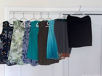 Six women's sleeveless summer tops and two knee-length pencil skirts hanging on hangers against white background for clear view of items and colors.