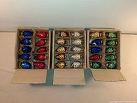 Three open boxes showing rows of 10 antique glass Christmas ornaments each in various colors: blue, red, gold, silver, green. Each has a textured honeycomb-like surface, original metal caps and hanging rings.