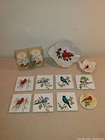 Ceramic items including printed bird tiles, cardinal bowl and teaspoon rest arranged together.