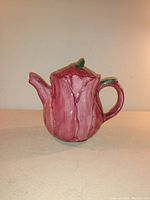 Front and side view of a pink and green ceramic teapot shaped like a cabbage, showing handle and spout.