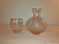 Photo of a set including a pink Depression glass bedside tumbler and matching carafe with floral etching, displayed against a plain background.