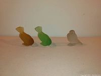 Three frosted glass sparrow figurines in amber, green, and clear, two in bowing posture and one standing, showing the overall set condition and colors.