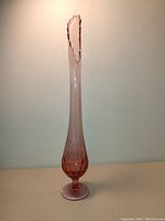 Front view of tall deep cranberry Fenton thumbprint swing vase showing elongated body, bulbous bottom with thumbprint texture, and scalloped swing lip rim.